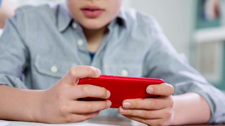 Niño sentado con celular rojo en mano